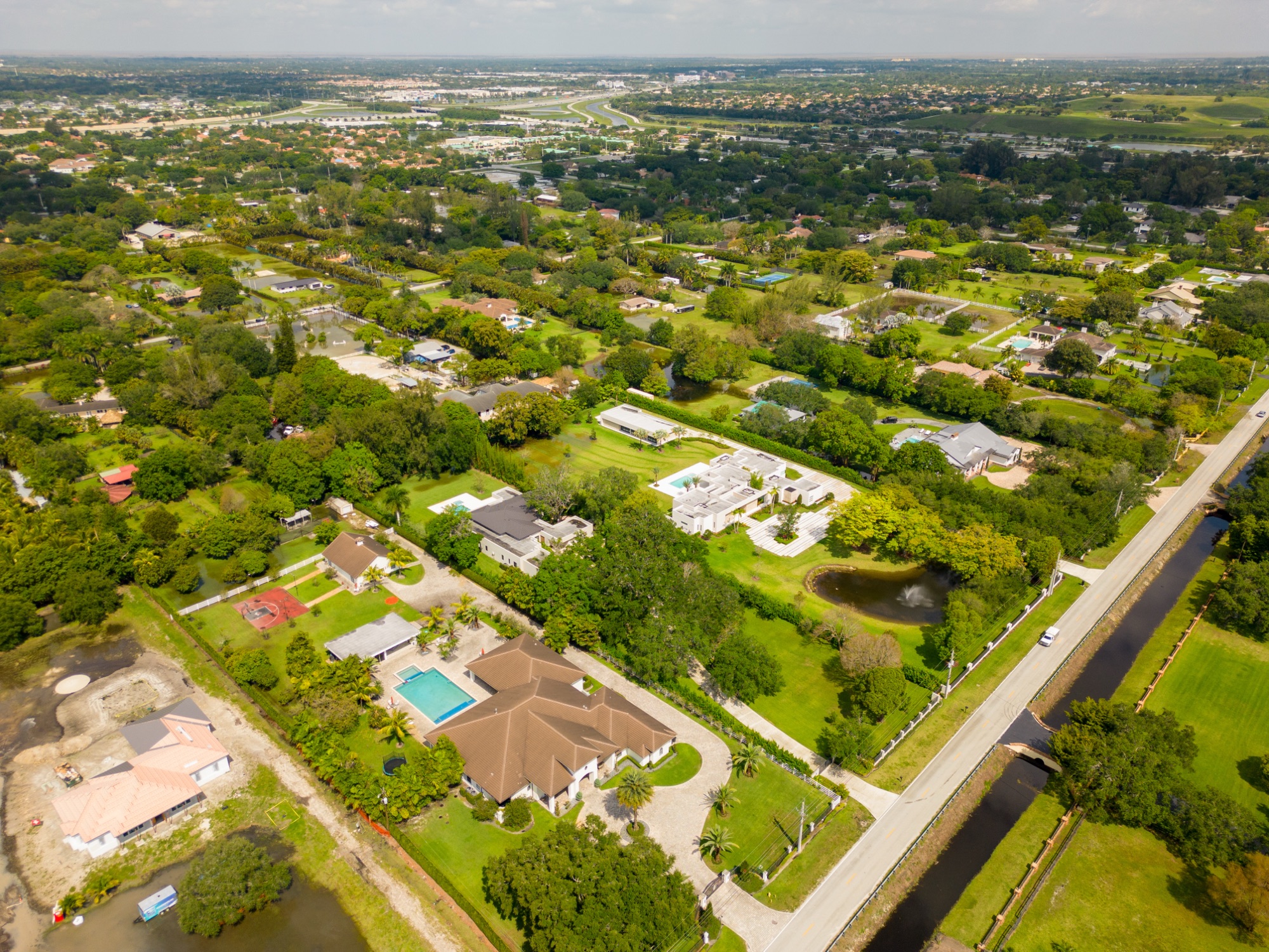 Aerial view of Southwest Ranches, Florida: acre-plus estates with pools and mature trees along a canal road